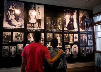 A couple stands in front of a wall with old photos from immigrants at Ellis Island