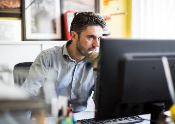 Hombre sentado frente a un escritorio mirando una computadora​​​​​​​