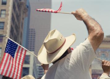 Un hombre con sombrero ondea una pequeña bandera estadounidense en un desfile