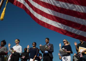 A group of people stand in front of the U.S. flag with their right hands up to take the oath