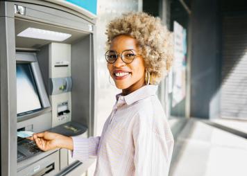 Una mujer negra parada frente a un cajero automático lista para usar su tarjeta bancaria