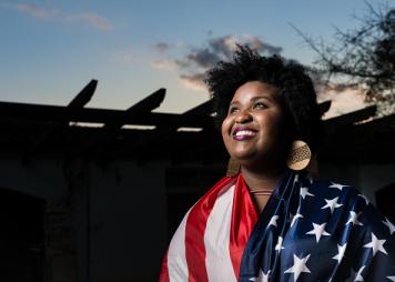 A black woman draped in the US flag smiling 