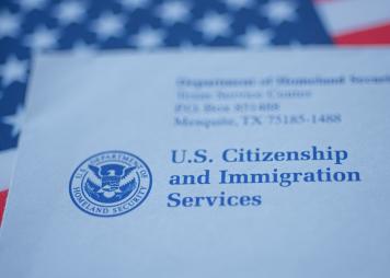 Hand touching Letter (Envelope) from USCIS on flag of USA background. Close up view.