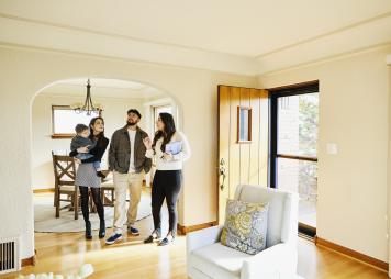 Toma amplia de una familia con un niño pequeño que habla con un agente inmobiliario mientras mira una casa en venta durante una jornada de puertas abiertas