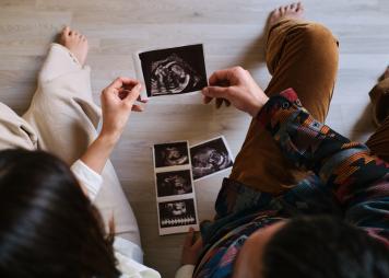 Couple sitting on the floor of their home look at their baby's ultrasound held by both of them.