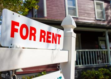 A white and red sign advertises a house for rent.