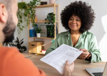 Young adult caucasian male job candidate giving resume to latin american female HR recruiter manager at work interview.