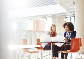 Two businesswomen talking and looking at the same laptop