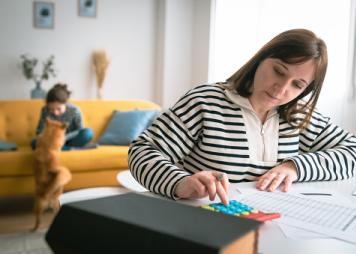 Mujer administrando el presupuesto familiar mensual mientras su hija juega con un perro en el fondo