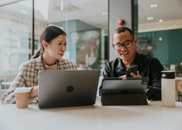 Dos personas hablando mientras usan sus computadoras portátiles