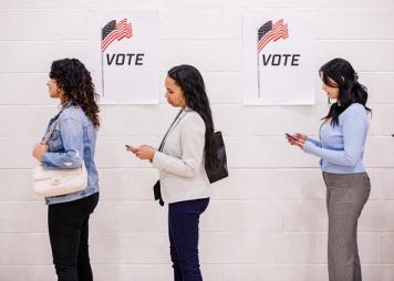 While waiting to vote, the young women stand quietly and use their mobile phones as they wait