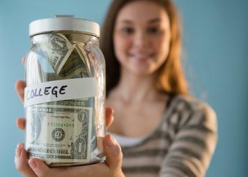 Niña hispana con un bote de ahorros para la universidad