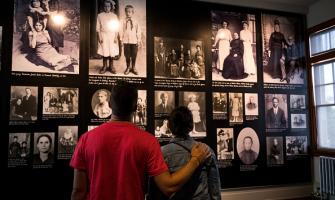 Una pareja de pie frente a una pared con fotos de inmigrantes en Ellis Island.