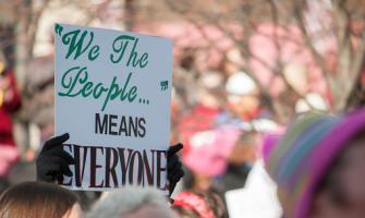 Manos recortadas sosteniendo un cartel que dice "'Nosotros, el pueblo' significa todos"
