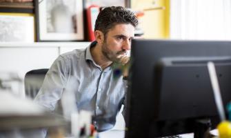 Hombre sentado frente a un escritorio mirando una computadora​​​​​​​