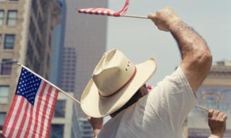 Un hombre con sombrero ondea una pequeña bandera estadounidense en un desfile