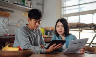 Una pareja asiática mira una computadora, y tiene papeles y comprobantes en su mesa