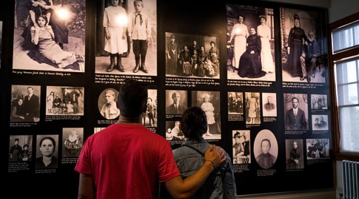 Una pareja de pie frente a una pared con fotos de inmigrantes en Ellis Island.