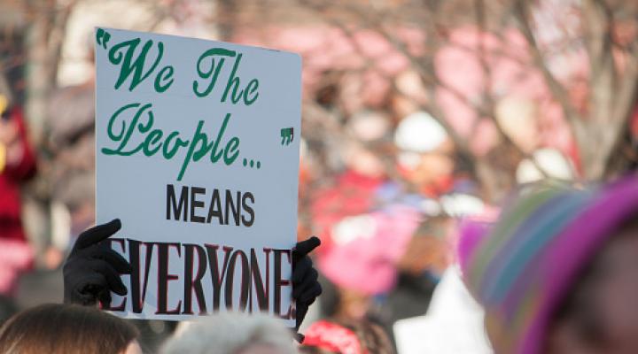 Manos recortadas sosteniendo un cartel que dice "'Nosotros, el pueblo' significa todos"