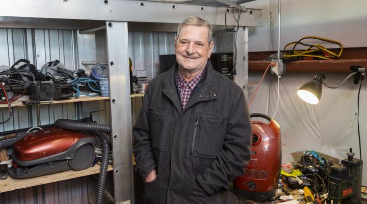 older man with a beard standing inside a tool shed looking at the camera