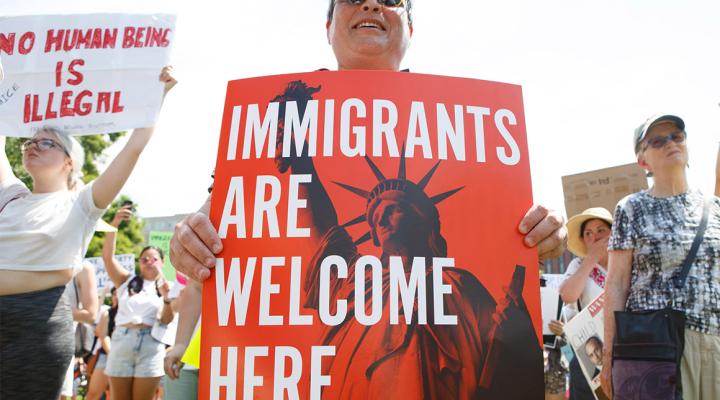 Mujer sosteniendo un cartel que dice "Immigrants Are Welcome Here"