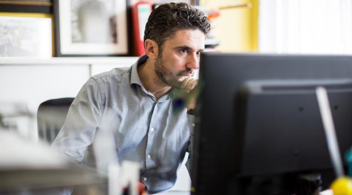 Hombre sentado frente a un escritorio mirando una computadora​​​​​​​