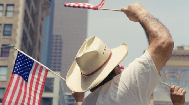 A man in a hat waving a small American flag at a parade