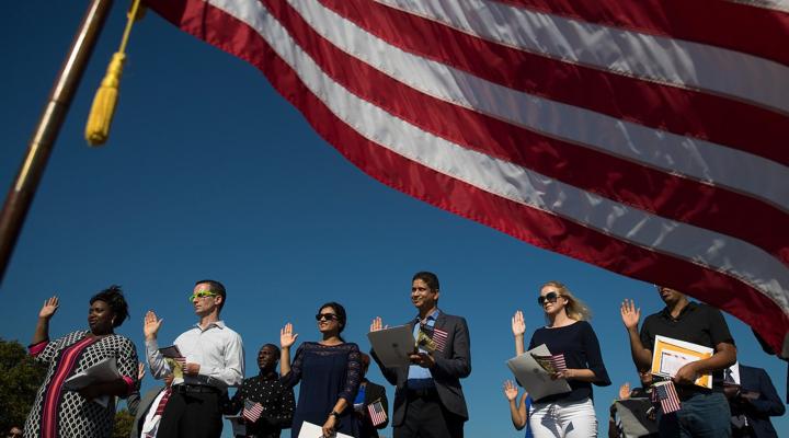 A group of people stand in front of the U.S. flag with their right hands up to take the oath