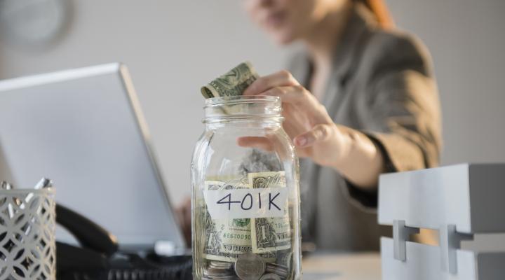 a woman puts a dollar into a glass jar with a label saying "401k" 