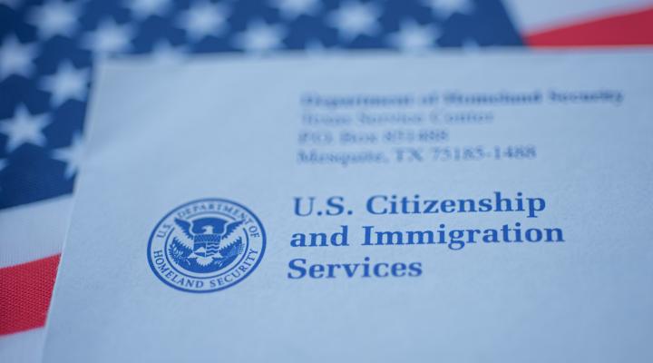 Hand touching Letter (Envelope) from USCIS on flag of USA background. Close up view.