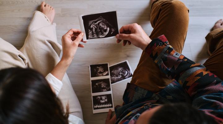 Couple sitting on the floor of their home look at their baby's ultrasound held by both of them.