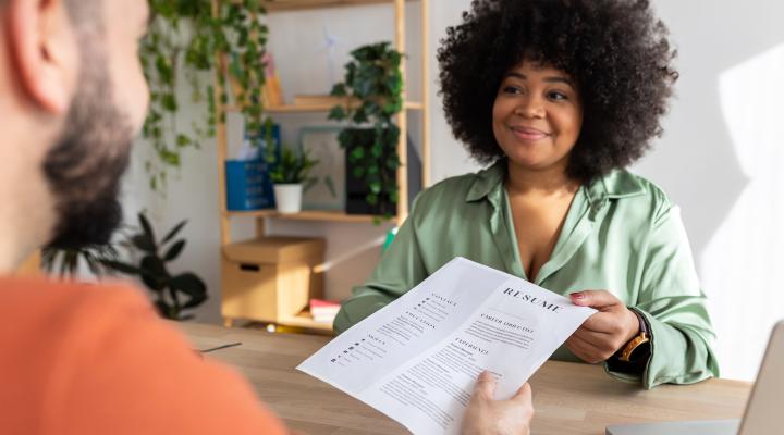 Young adult caucasian male job candidate giving resume to latin american female HR recruiter manager at work interview.