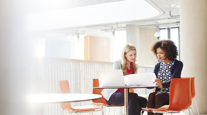 Two businesswomen talking and looking at the same laptop