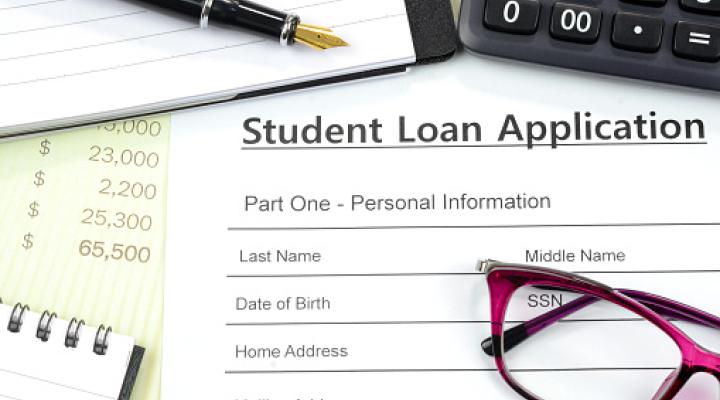 Solicitar un préstamo estudiantil. Completar el formulario de préstamo con calculadora, lapicera y bloc de notas sobre la mesa.