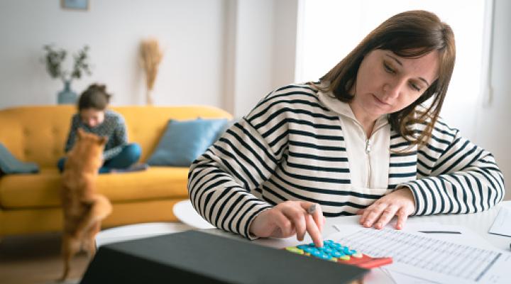 Woman managing the monthly family budget while her daughter plays with a dog in the background