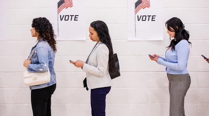 While waiting to vote, the young women stand quietly and use their mobile phones as they wait