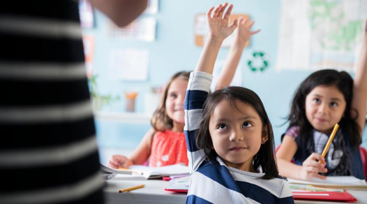 Niñas levantando la mano a la maestra en clase
